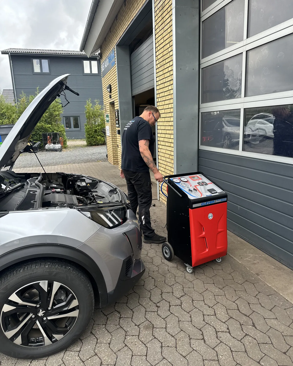 Bil klar til airconditionservice foran MB Autotekniks værksted med A/C-servicestationen ved porten